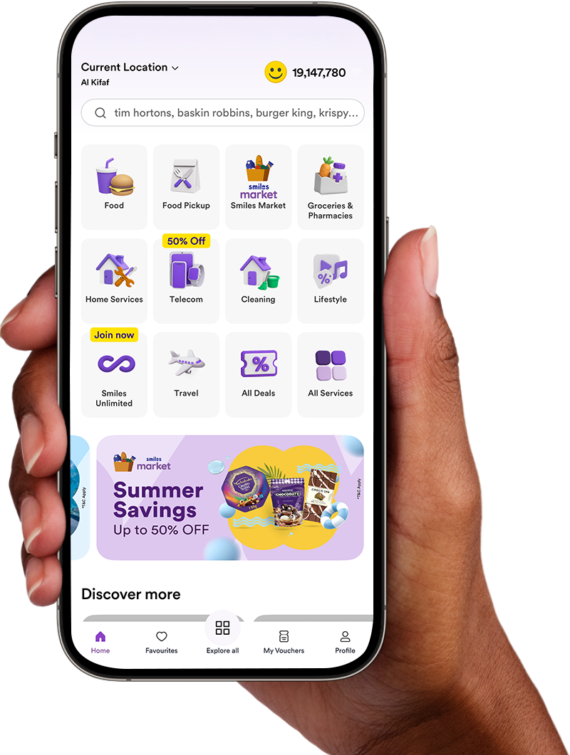 Hand holding a smartphone displaying the Smiles app home screen, showing categories like Food Delivery, Smiles Market, Groceries & Pharmacies, Home Services, Telecom, Cleaning, Lifestyle, Smiles Unlimited, Travel, and All Deals. The screen also features a banner for Smiles Market Summer Savings with up to 50% off. Smiles Points balance displayed at the top.