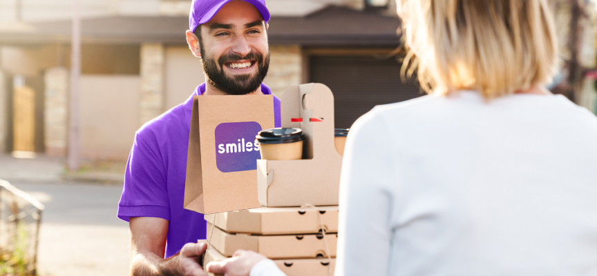 Smiling delivery courier wearing a purple uniform handing over a restaurant food delivery order to a customer in Dubai.