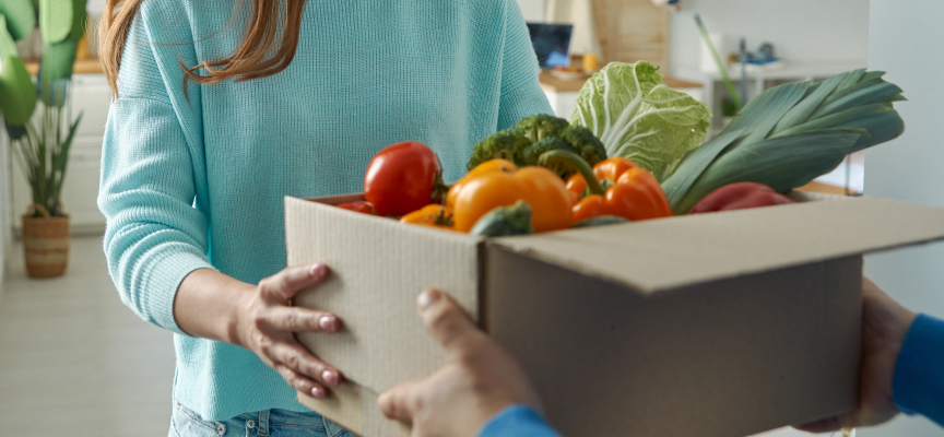 Delivery driver handing over a cardboard box filled with fresh market produce directly to a customer in the UAE.
