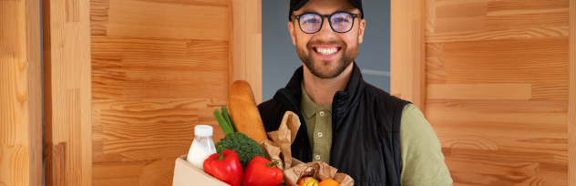 Smiling delivery courier holding a grocery bag filled with fresh bell peppers and bread representing Smiles home grocery delivery services.