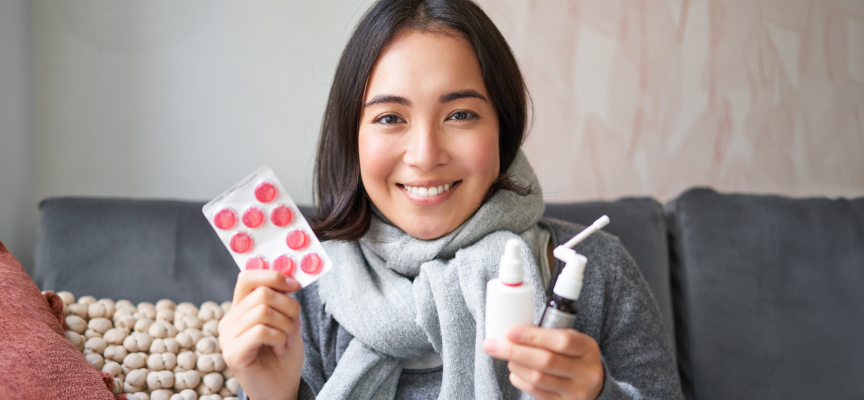 Smiling woman holding medicine blister packs and cold remedy sprays illustrating fast home medicine delivery in Dubai.