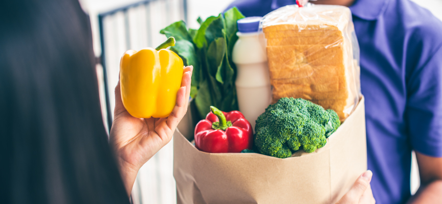  Delivery driver handing a brown grocery paper bag filled with fresh produce and bell peppers directly to a customer.