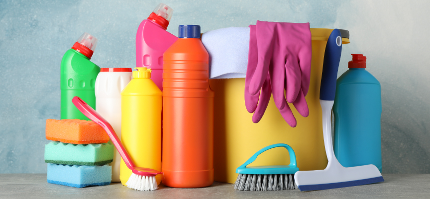 Array of household cleaning supplies including detergents, plastic spray bottles, brushes, and rubber gloves for online service booking.