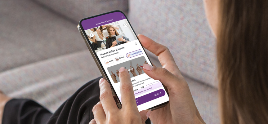 Customer holding a smartphone and browsing the Smiles house maintenance app to select professional home cleaning or beauty services.