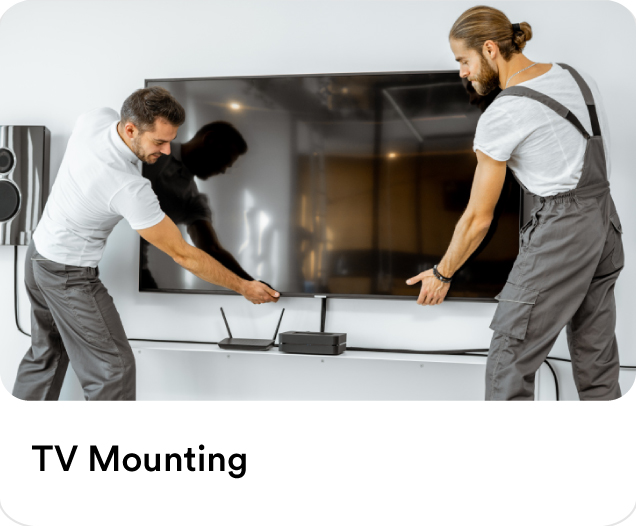 Two handymen carefully fixing a large flat-screen television to a living room wall for professional TV mounting services.