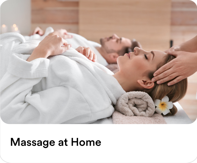 A man and woman relaxing in white robes while receiving a professional head massage during a couples massage at home session.
