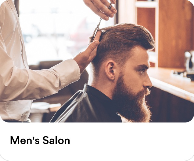 Professional barber cutting a man's hair and grooming his beard to illustrate premium men's salon at home services in the UAE.