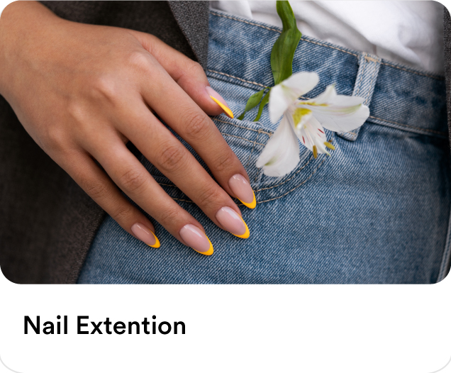 Close-up of a woman's manicured hand with yellow French tips on denim jeans showcasing professional home nail extensions and manicure services.